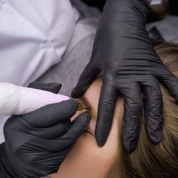 Hands of the master in black sterile gloves that perform permanent eyebrow makeup. PMU Procedure, Permanent Eyebrow Makeup.