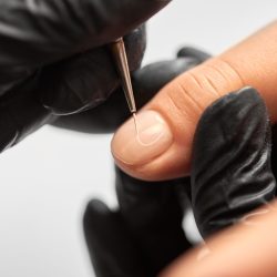 Process of making fashionable manicure in beauty salon. Close-up of professional master manicurist hands painting patterns on client woman nails using applicator on light blurred background.