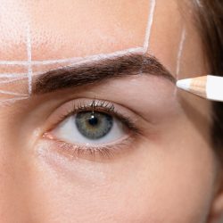 Young woman during professional eyebrow mapping procedure before permanent makeup